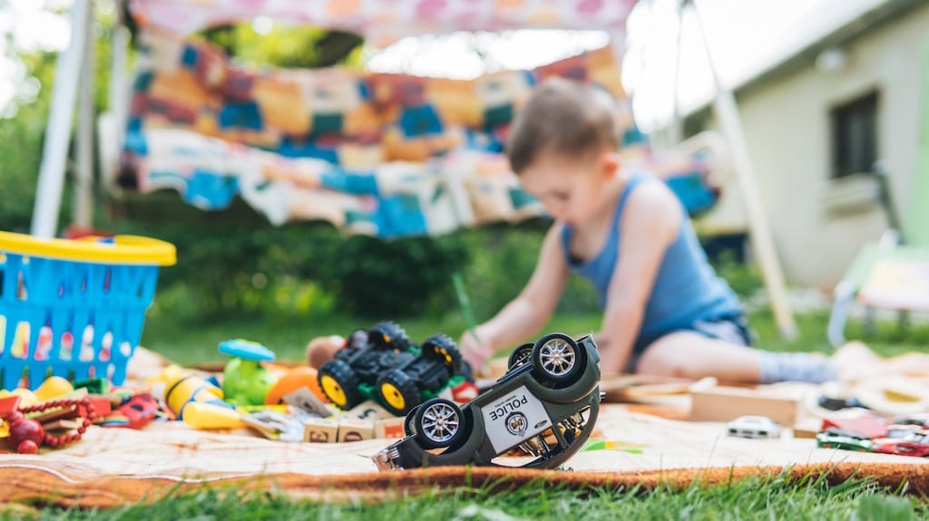 Child playing outside on the lawn with trucks, blocks paints and other toys.